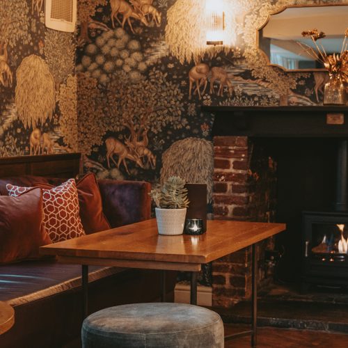 The Three Horseshoes cosy corner in the bar area, with a log burner fire place and beautiful flora and fauna inspired wallpaper.